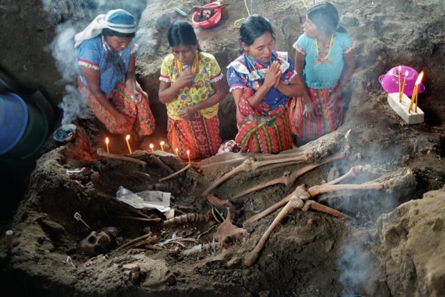 Guatemalan aboriginal woman praying in front of remains of executed by the army during the civil war burriend inside a church